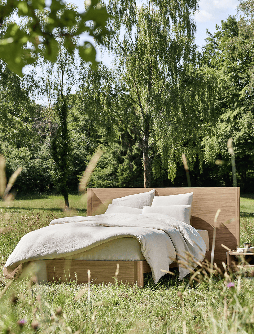 Lit en bois massif Kipli installé en pleine nature, avec linge de lit en lin naturel, illustrant une chambre écologique et un sommeil sain au cœur d’un environnement verdoyant.