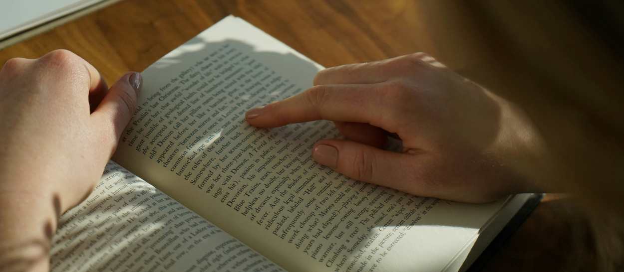 Gros plan sur des mains feuilletant un livre dans un coin lecture éclairé par la lumière naturelle.