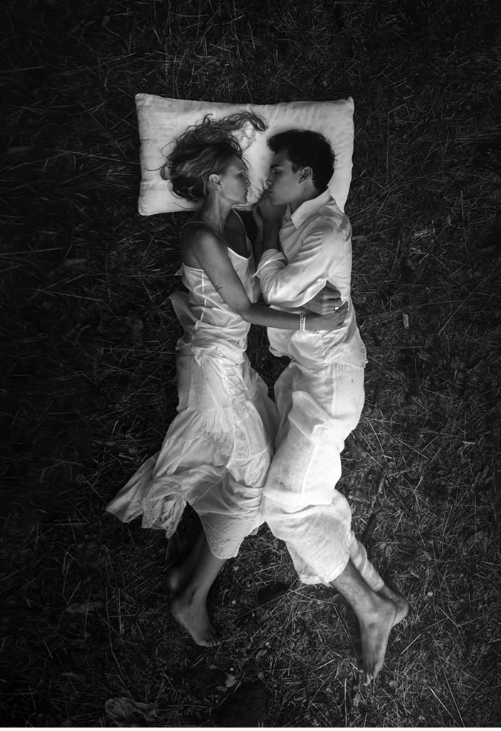 Deux personnes allongées l’une contre l’autre dans l’herbe sur un oreiller, illustrant un moment de détente, de connexion et de sommeil naturel en plein air.