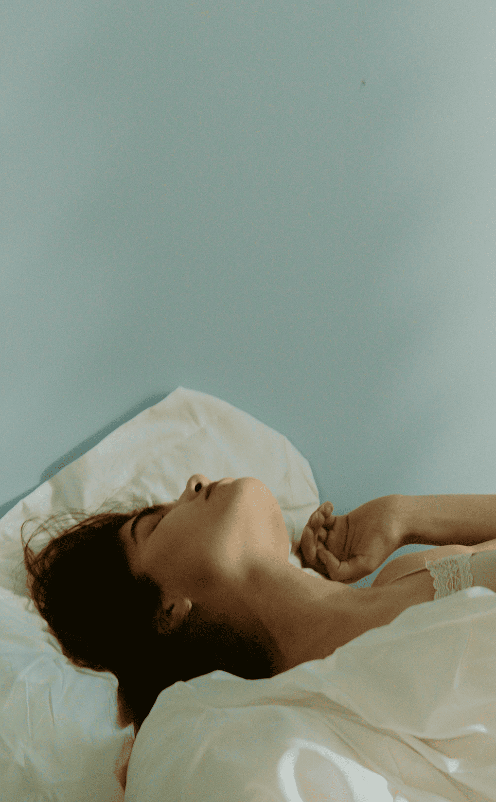 Femme endormie paisiblement dans un lit lumineux, illustrant un sommeil réparateur et une ambiance de chambre apaisante.