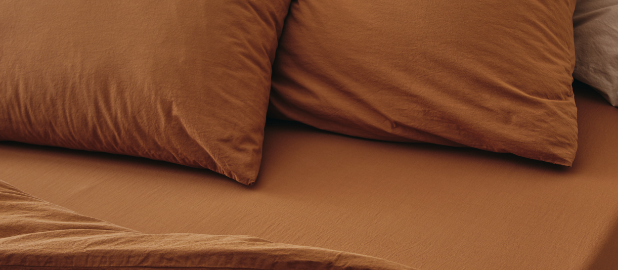 Linge de lit en coton biologique couleur terracotta sur un lit Kipli, illustrant un intérieur chaleureux et des textiles naturels pour une chambre saine.