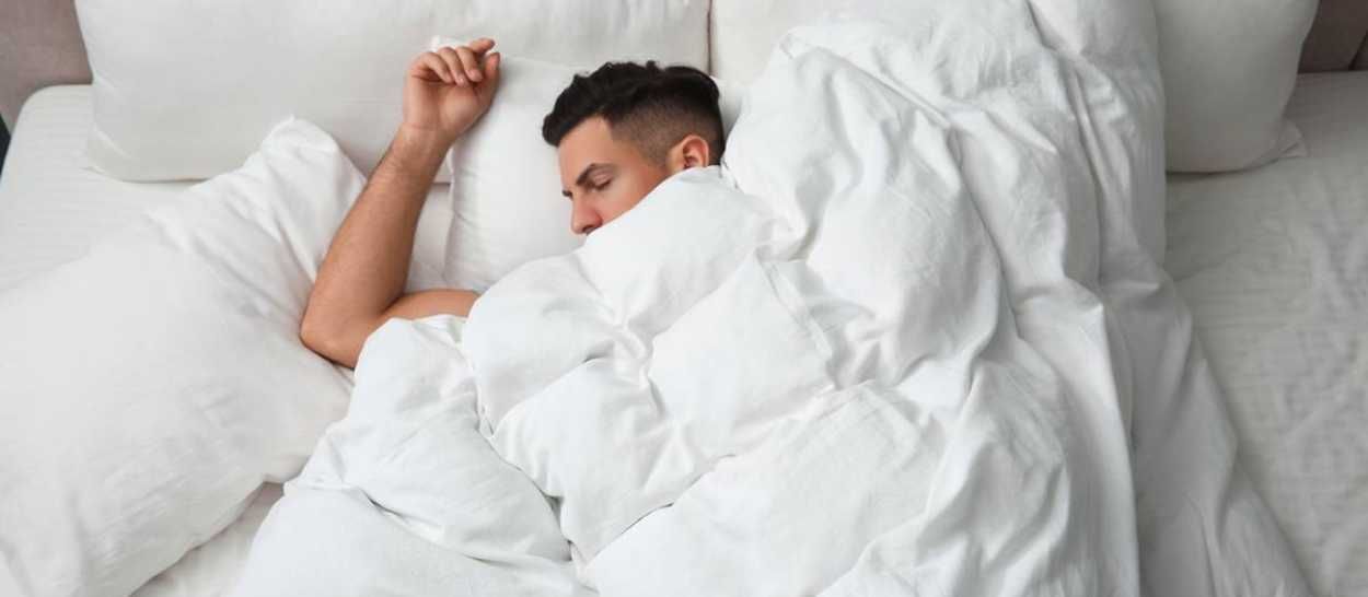 Homme dormant profondément dans un lit douillet illustrant le besoin de dormir plus longtemps en hiver.