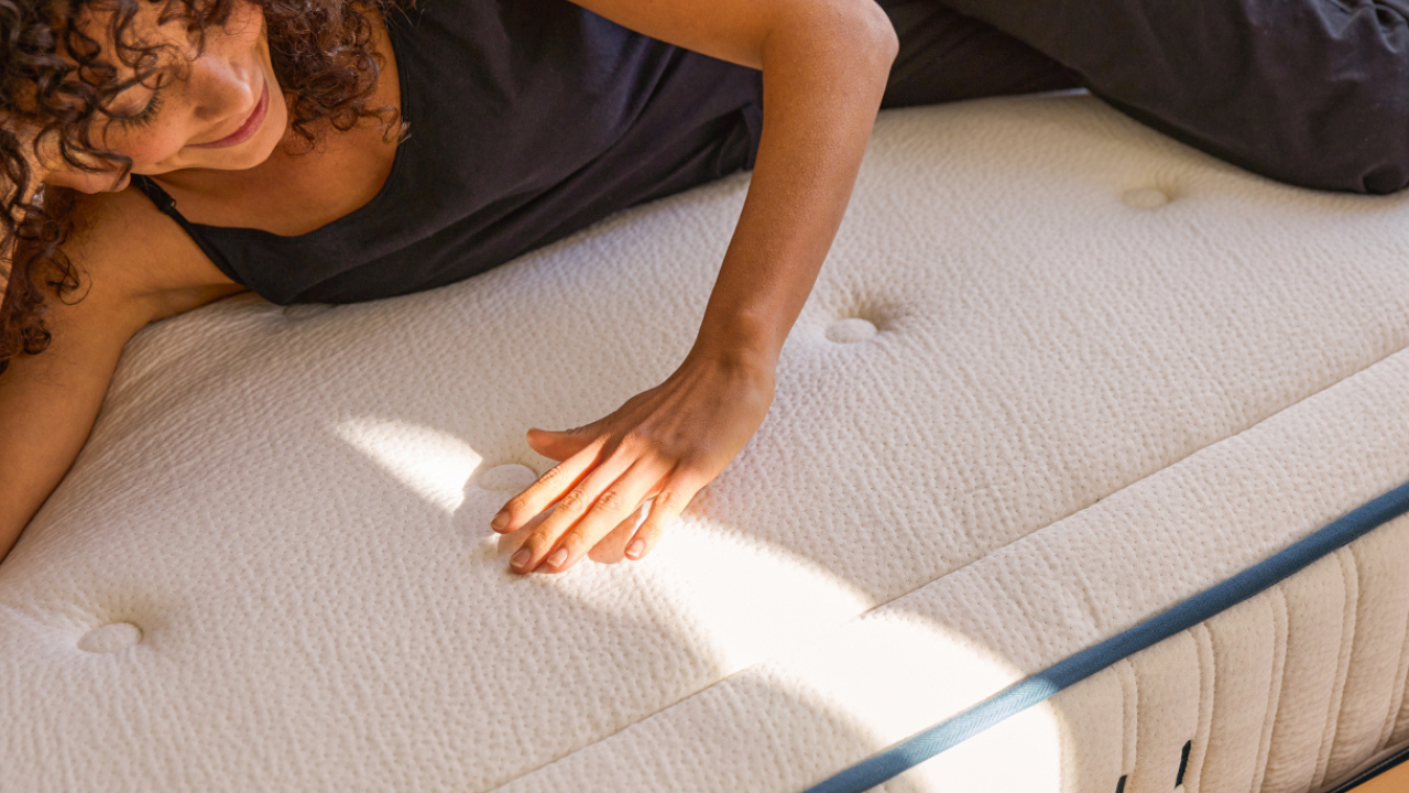 Femme testant le confort d’un matelas en latex naturel Kipli, main posée sur la surface moelleuse pour illustrer la qualité, le soutien et le bien-être au naturel.