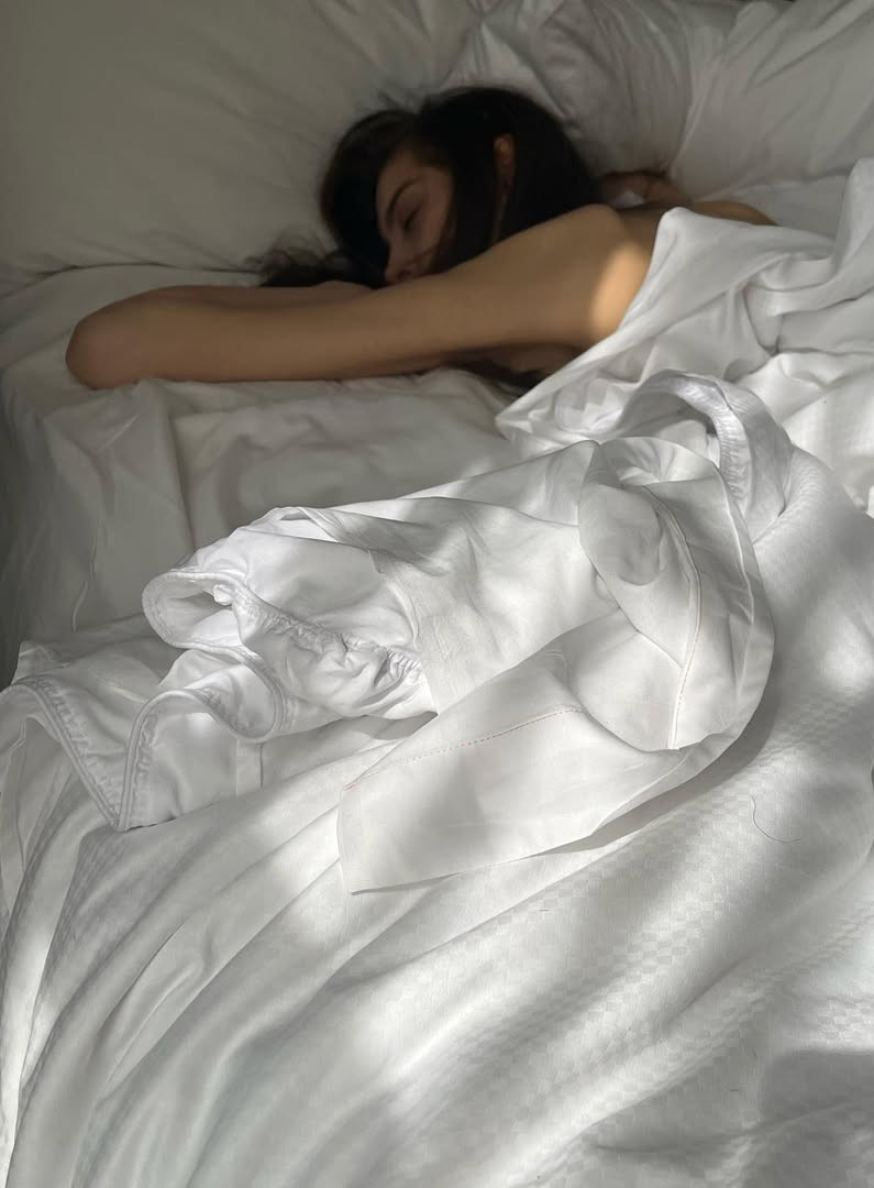 Personne endormie dans des draps blancs baignés de lumière naturelle, illustrant un sommeil réparateur et une literie confortable et apaisante.