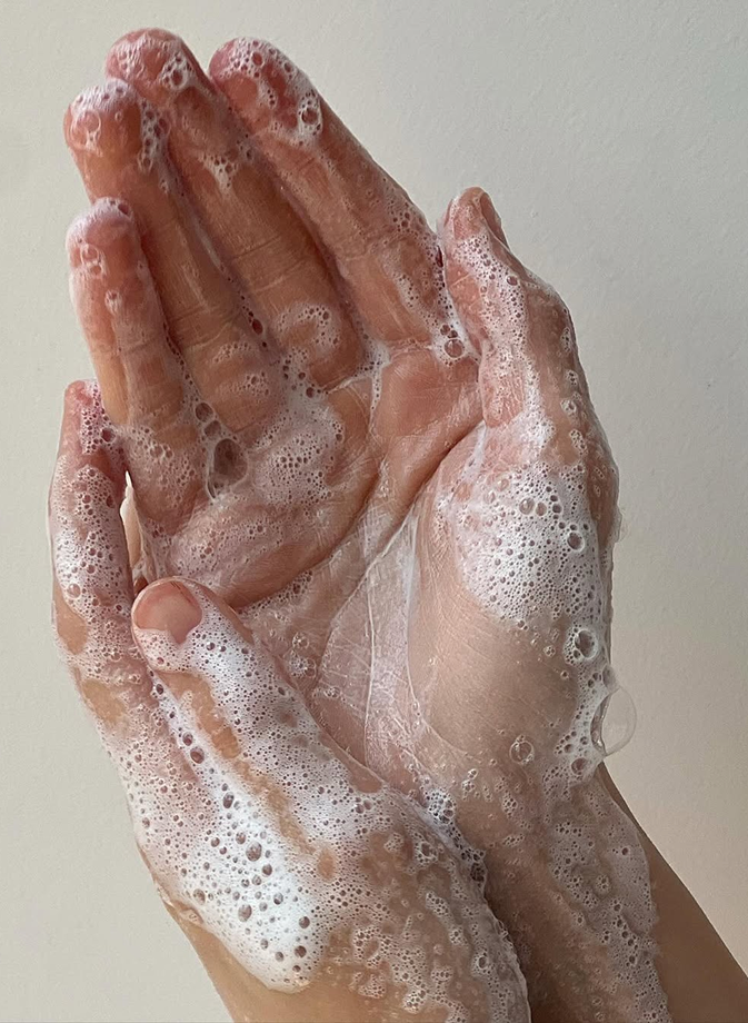 Mains savonneuses recouvertes de mousse, illustrant un geste de nettoyage doux et naturel pour entretenir sa literie et préserver un environnement de sommeil sain.