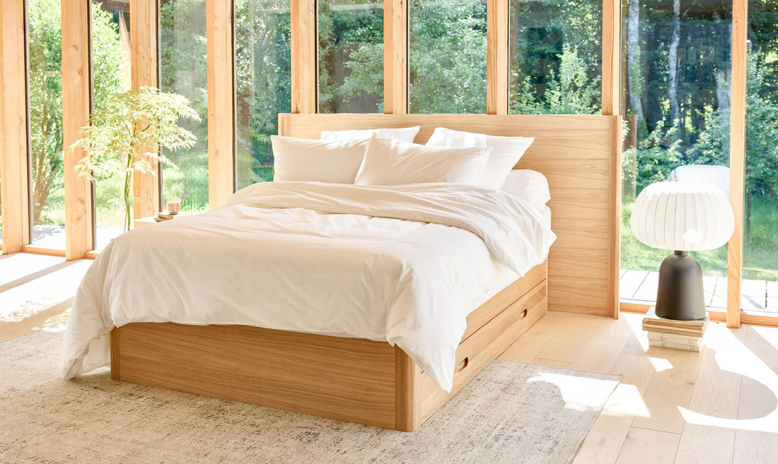 Chambre lumineuse avec lit en chêne à tiroirs Kipli, draps blancs et lumière naturelle traversant de grandes baies vitrées.